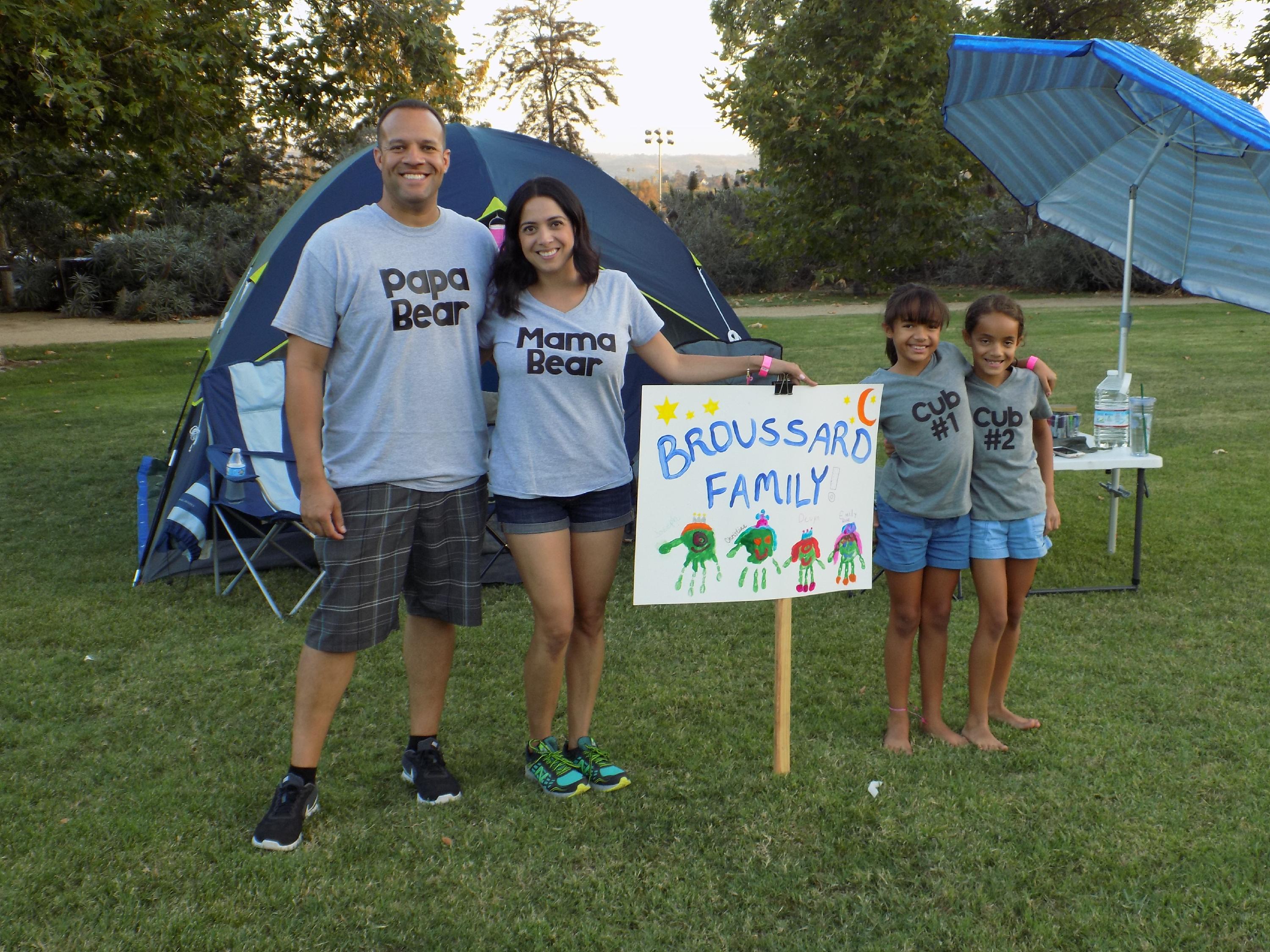 A family of four stands together in a green field